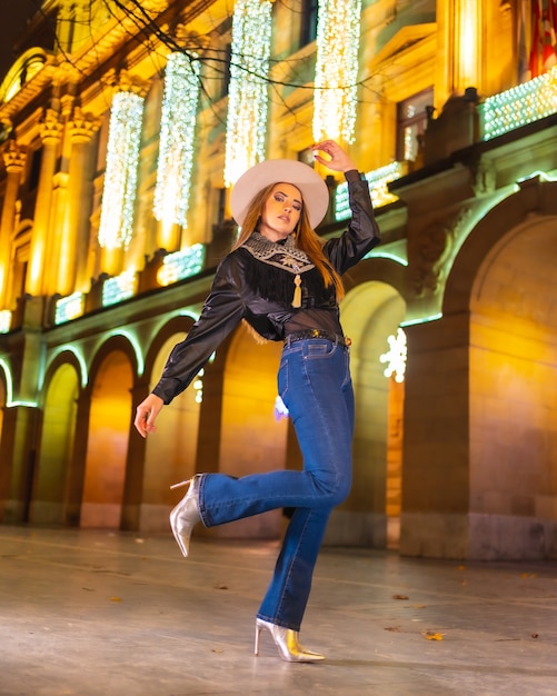 Winterlevensstijl, jong Kaukasisch blond model met jeans en een zwarte jas in de stad verlicht voor Kerstmis 's nachts