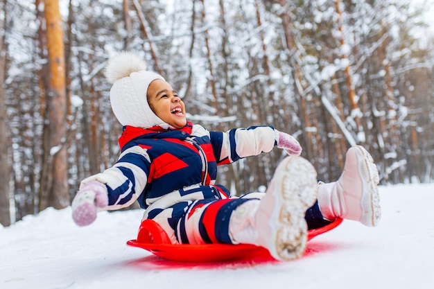 Winterportret van een gelukkig klein meisje met een gebreide muts en een jumpsuit buiten in de winter
