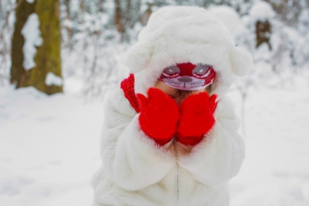 Winterportret van een meisje in een witte bontjas en een rode sjaal in een besneeuwd bos