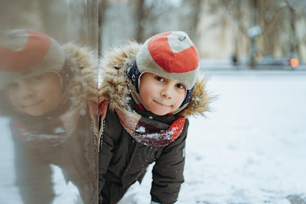 Winterportret van schattige blanke jongen van elementaire leeftijd in gebreide muts met pompon in de stad