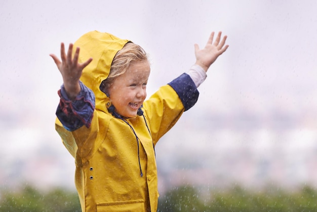 Winterregenjas en een meisje dat plezier heeft in het water buiten alleen spelen tijdens het koude seizoen Kinderen regenen of nat met een schattig klein vrouwelijk kind dat overdag met uitgestrekte armen buiten staat