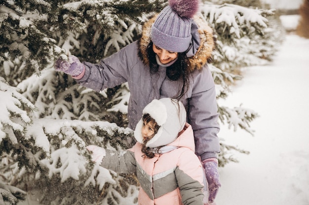 Winterse openluchtrecreatie. Gelukkige moeder schudt sneeuw van een tak op een kind dat tussen besneeuwde sparren staat