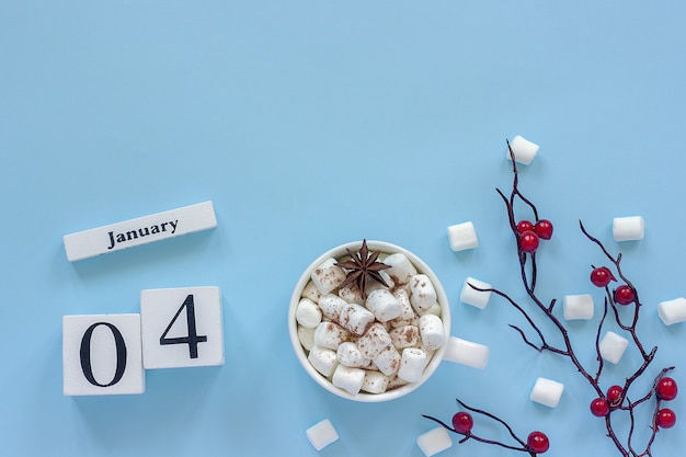 Winterse samenstelling. witte houten kalenderblokjes. gegevens 4 januari kopje cacao, marshmallows en decoratieve tak met rode bessen op blauwe achtergrond bovenaanzicht plat leggen kopieerruimte