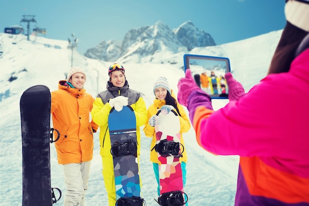 wintersport, technologie, vrije tijd, vriendschap en mensen concept - gelukkige vrienden met snowboards en tablet pc-computer nemen foto over sneeuw en berg achtergrond