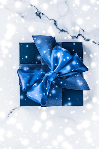 Wintervakantie geschenkdoos met blauwe zijden strik sneeuwglitter op marmeren achtergrond als kerst- en nieuwjaarscadeautjes voor flatlay-ontwerp van luxe schoonheidsmerk