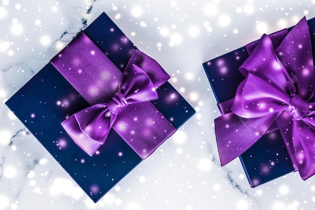 Wintervakantie geschenkdoos met paarse zijden strik sneeuwglitter op marmeren achtergrond als kerst- en nieuwjaarscadeautjes voor luxe schoonheidsmerk flatlay design