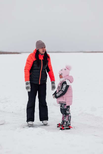 Winterwandeling in de natuur jonge vrouw en klein meisje schaatsen op bevroren rivier moeder en dochter