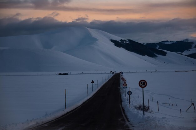 Winterweg in de schemering na zonsondergang omringd door bergen bedekt met sneeuw