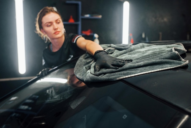 Фото Протирает поверхность полотенцем современный черный автомобиль чистит женщина внутри автомойки