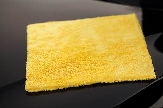 Foto pulendo il pannello di un'auto di lusso con microfibra gialla