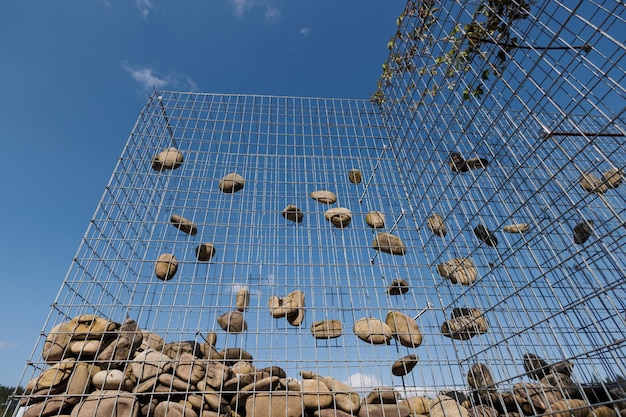 Wire Rock Fence Stone wall texture rocks behind metal grid fence background and beautiful blue sky