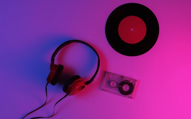 Wired headphones, vinyl record, audio cassette with neon
blue-red gradient light. retro wave, 80s pop culture. top view