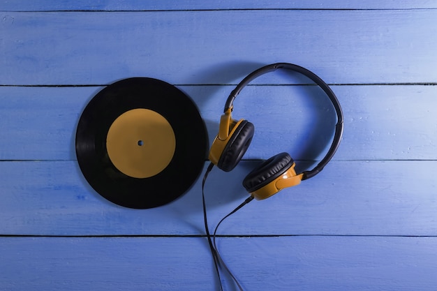 Wired headphones and vinyl record on blue wooden background. Retro wave, 80s pop culture. Top view
