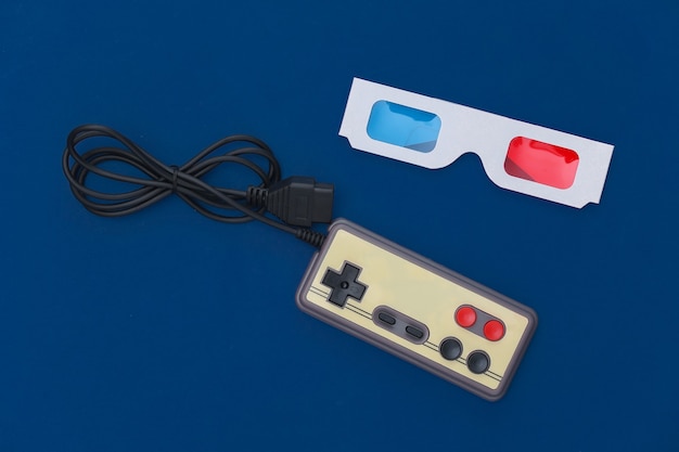 Photo wired retro gamepad and anaglyph 3d glasses on a classic blue background. retro attributes, 80s. top view