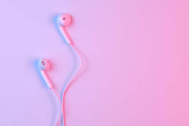 Wired white earphones isolated on white background closeup in\
pink neon light