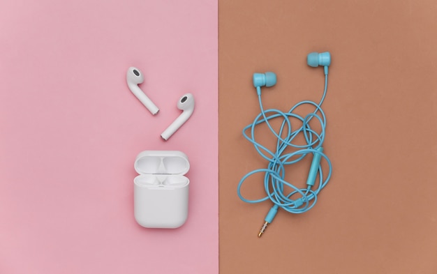 Photo wireless earbuds and wired tangled earphones on brown pink background. top view. flat lay