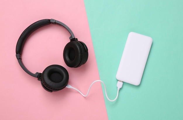 Photo wireless headphones and external portable battery power bank on pink blue background top view flat lay