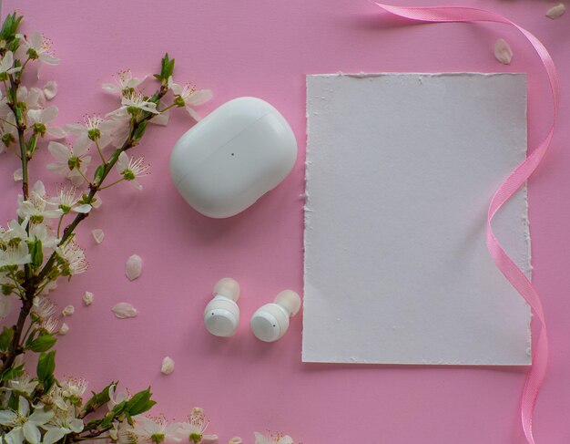 Wireless headphones on pink background with cherry flowers and copy space