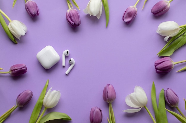 Wireless headphones pods and spring tulips on violet background