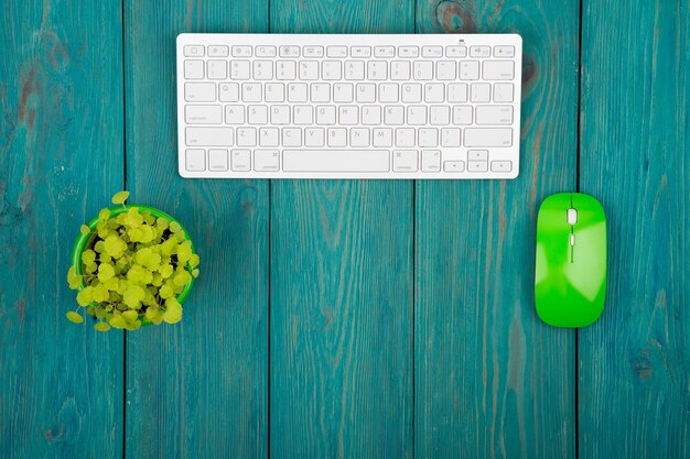 Wireless slim white keyboard and green mouse on blue wooden desk