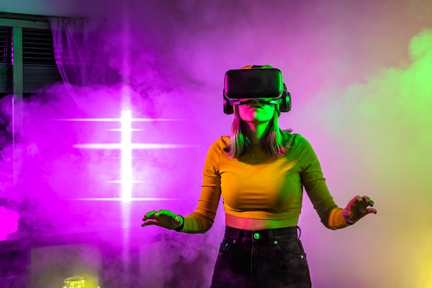 Wireless technologies young woman using virtual reality glasses in the room with neon lighting