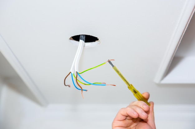 Wires and holes for light bulb in the ceiling Man holding screwdriver Electricity maintenance repair works in the flat Restoration indoors