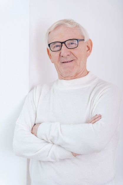 Wise and confidence. Confident senior man keeping arms crossed and smiling at camera while leaning at the wall