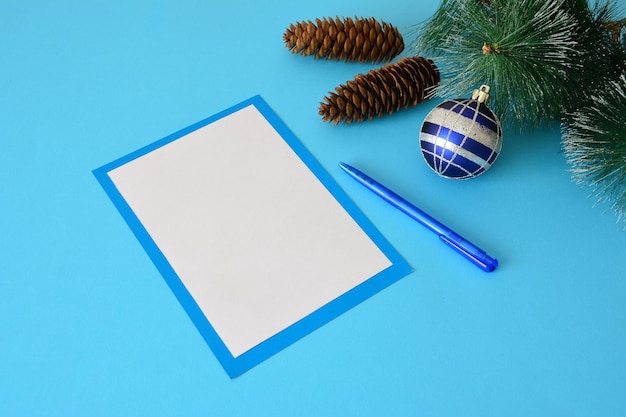 список пожеланий с ручкой, сосновой веткой, шишками и рождественской сферой, крупным планом
