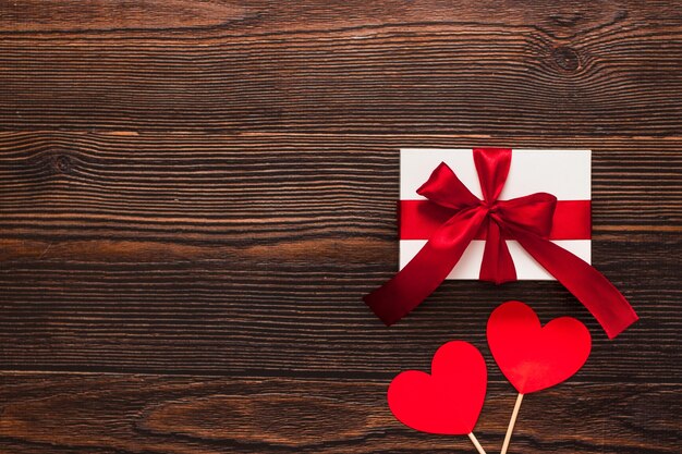 Wit aanwezig met een rood lint en papieren harten geïsoleerd op een donkere houten achtergrond. Bovenaanzicht van een feestende warme flatlay. Valentijnsdag en kerst concept. Copyspace.