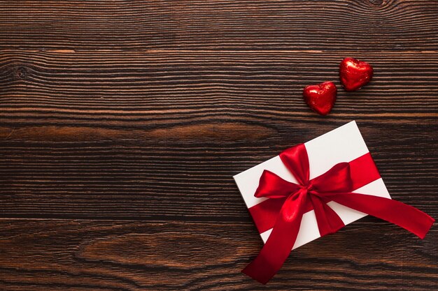 Wit aanwezig met een rood lint en twee chocolade rode harten geïsoleerd op een donkere houten achtergrond. Bovenaanzicht van een feestende warme flatlay. Valentijnsdag en kerst concept. Copyspace.