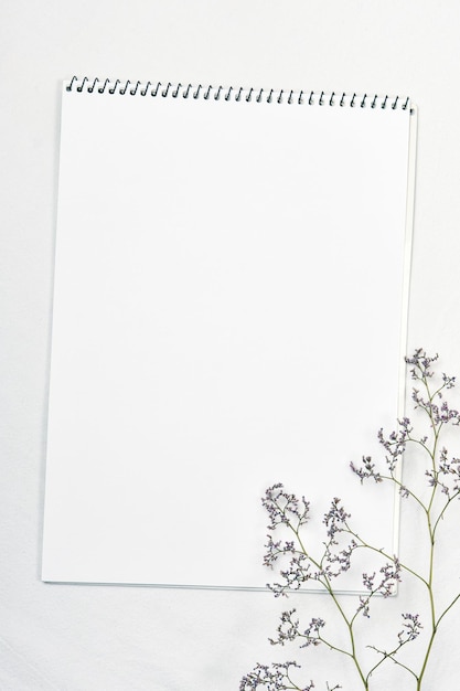Wit aquarel schetsboek en een takje wilde kermek op een linnen tafelkleed
