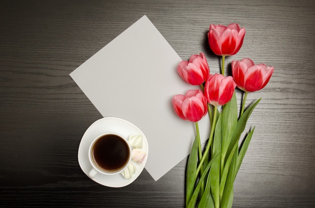 Wit blanco vel papier, roze tulpen en een mok koffie. Zwarte tafel. bovenaanzicht