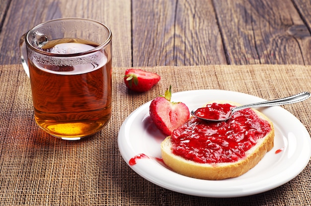 Wit brood met aardbeienjam en kopje thee op houten tafel