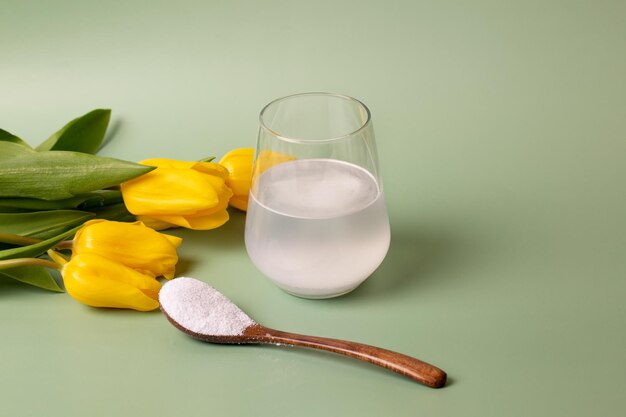 Wit collageenpoeder in een transparant glas met water en een houten lepel op een groene achtergrond