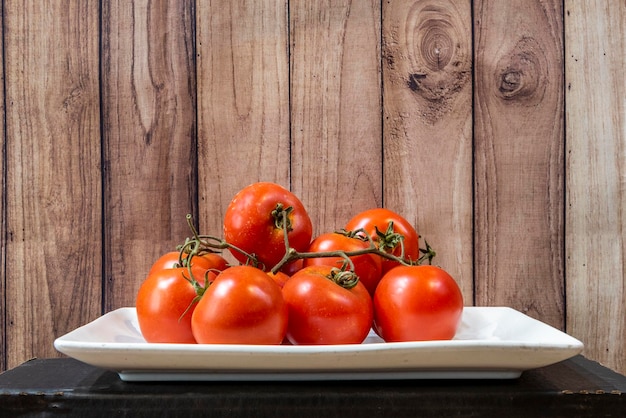 Wit dienblad met snaren van rijpe ronde tomaten op houten achtergrond