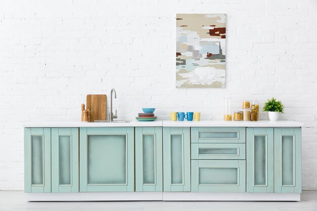 Wit en turquoise keukeninterieur met keukengerei en abstract schilderij op bakstenen muur
