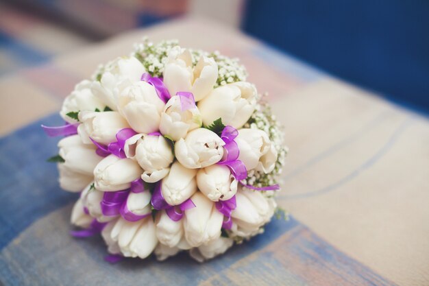 Wit huwelijksboeket van tulpen met purper lint op bank