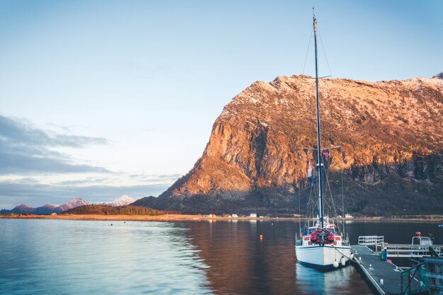 Wit jacht met een lange mast afgemeerd aan de drijvende ponton in de Noorse fjord. Zonsondergang