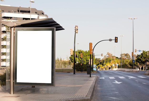 Wit leeg verticaal reclamebord bij de bushalte op de stadsstraat op de achtergrond van bussen en ro