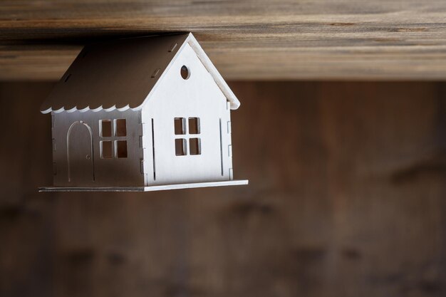 Foto wit model van een huis dat ondersteboven op een driehoekig dak staat op een bruine houten ondergrond. vastgoed concept