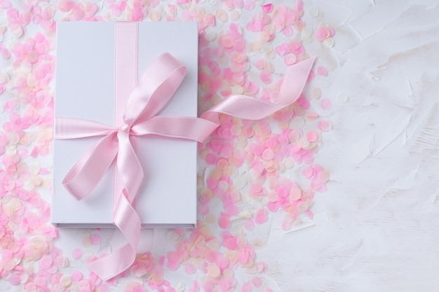 wit oppervlak met cadeau, witte doos met roze lint op roze confetti.