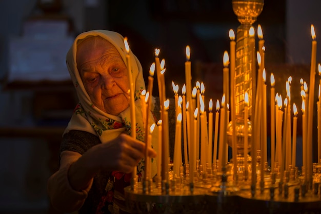 Wit-Rusland, Homel, 19 januari 2019. Kerk van St. George. Oude grootmoeder in de kerk zet een kaars. Oudere Russische vrouw met hoofddoek in kerk
