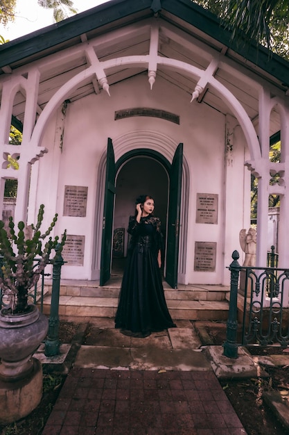 A witch in an all black dress and scary makeup was standing at the cemetery gate