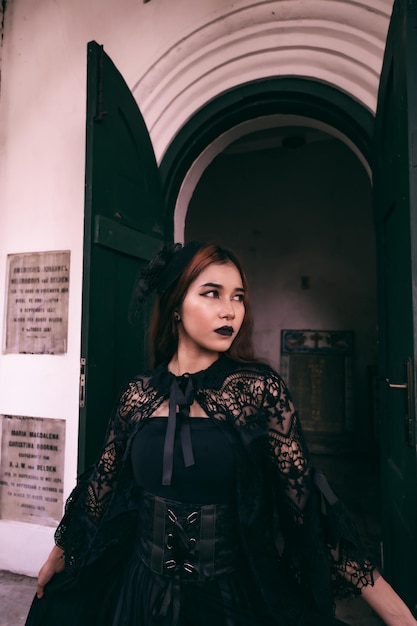 A witch in an all black dress and scary makeup was standing at the cemetery gate