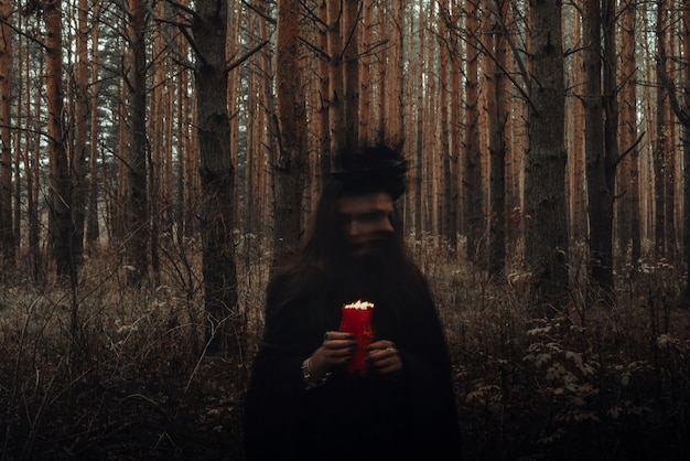 Witch in a black costume performs dark spells with candles in the forest. Blurry photo with blurring due to long exposure time