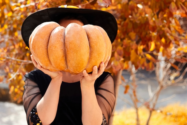 A witch covering her face with orange pumpkin.