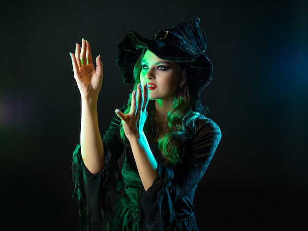 A witch creates magic a young beautiful brunette in a pointed hat