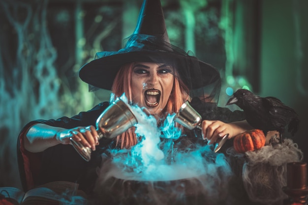 A witch in foggy surrounding holds two goblets above boiling water for a cooking poison soup.