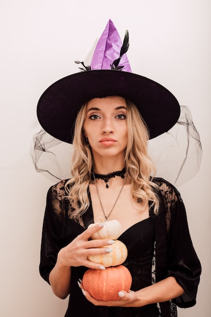 A witch in a purple hat holds pumpkins in her hands