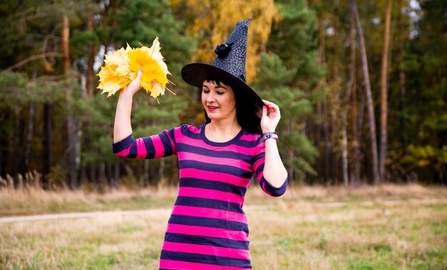 La strega lancia le foglie nella foresta autunnale. halloween festa in costume mago donna